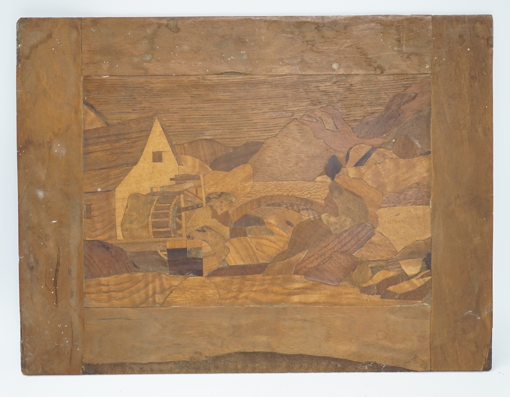 From the Studio of Fred Cuming. An inlaid marquetry panel depicting a watermill before mountains, 30 x 40cm. Condition - poor to fair
